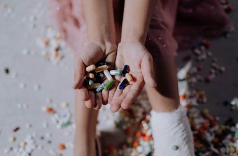 Close-up of a child holding pills with an injured leg in a cast, symbolizing health and recovery.