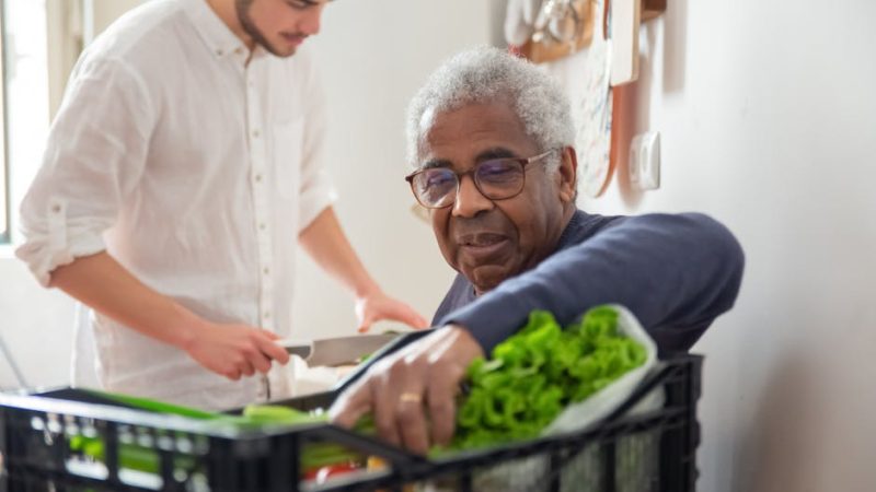 A senior man supported by a volunteer with groceries at home.
